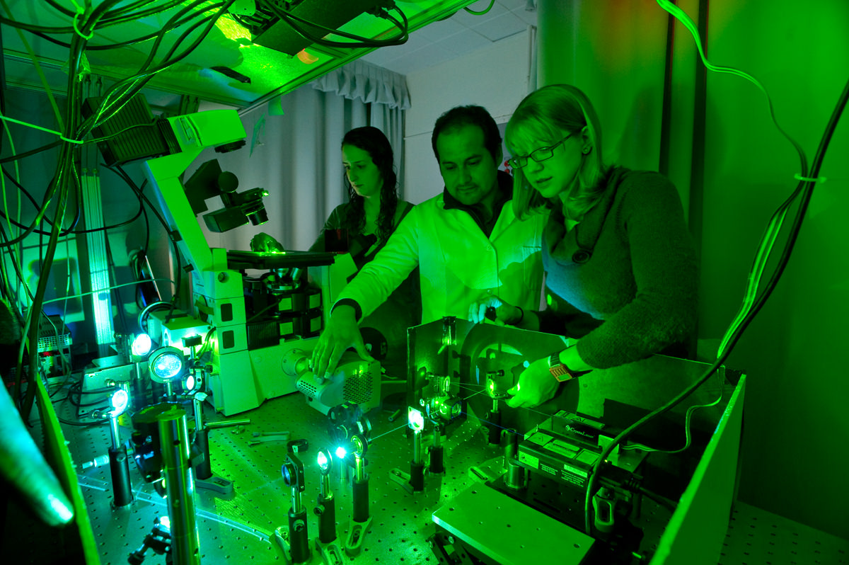 Ross works with postdoc,  Daniel Diaz-Valencia (middle), and graduate student, Leslie Conway (back), on the total internal reflection fluorescence microscope for single molecule imaging. Image courtesy of Jim Gipe, Pivot Media.
